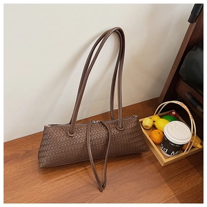 Detail showing the woven leather texture and brown baguette shoulder bag on a wooden table