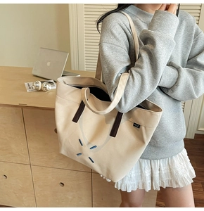 Detail of minimalist beige canvas tote bag with leather straps and embroidered smile design