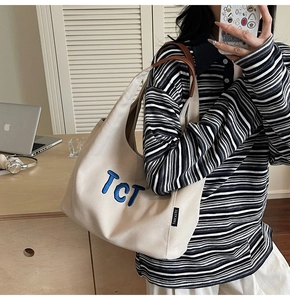 Detail of canvas tote bag featuring brown leather handles and blue embroidered TCT text