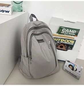 Detail of grey nylon backpack with wrinkled texture, multi-zipper layers and side pocket