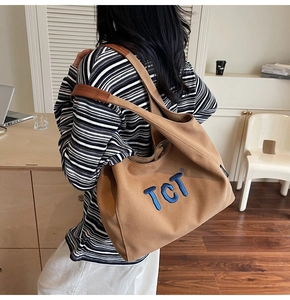 Detail showing thick cotton canvas texture and 3D blue embroidered TCT logo on caramel tote