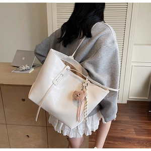 Detail view of white crocodile pattern tote bag with brown plush bear charm and shoulder strap