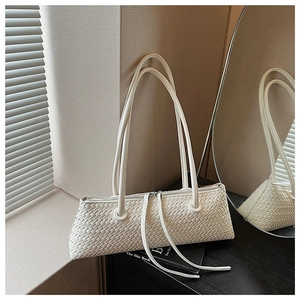 Detailed view of woven texture and fringe zipper pull on a cream underarm baguette bag