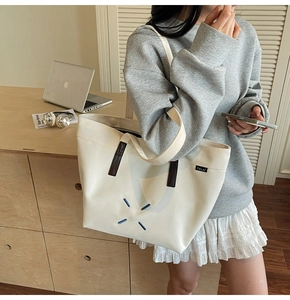 Detail of white canvas tote bag featuring blue X-stitching and brown leather accents