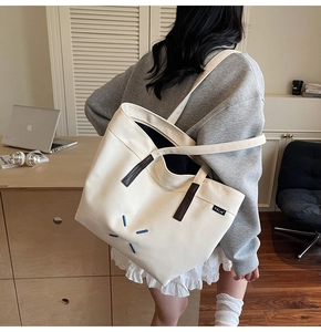 Side view of a large canvas tote bag with brown leather straps shown on a model
