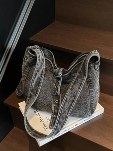 Retro black wash denim tote bag with metal grommets and wide strap on wooden stairs