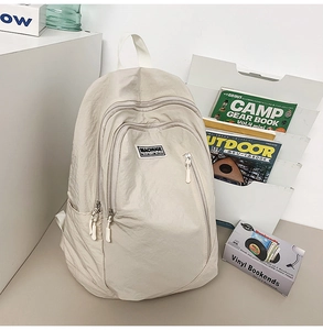Detail of beige nylon backpack showing multiple zipper pockets and smooth fabric texture