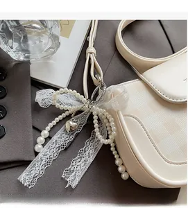 Eleganter Perlen- und Spitzenbogenanhänger mit Herzanhänger an einer beigen Handtasche