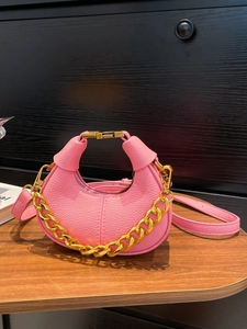 Pink crescent handbag with lychee texture and gold chain on wooden desk
