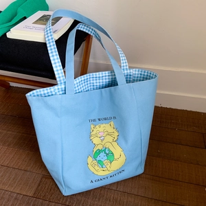 Detail of light blue canvas tote bag with cat print and blue plaid handles on wood floor