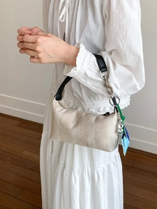 Beige woven handbag with black leather strap and colorful charms worn by model