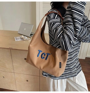 Close-up of brown canvas tote bag with TCT embroidery and leather handles in a home office