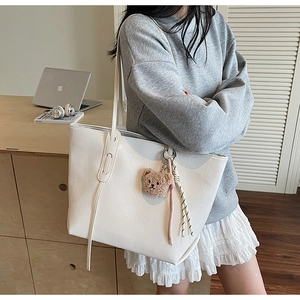 Detail of white tote bag with faux crocodile pattern and cute bear charm worn by a model