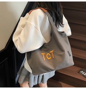 Close-up of grey canvas tote bag with orange TCT embroidery and branded side label detail