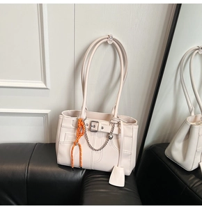 Dettaglio di una borsa tote beige con fibbia e corda arancione su un divano