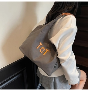 Detail of grey canvas tote bag with orange embroidery and brown leather shoulder straps
