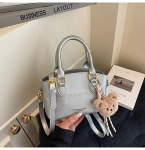 Close-up of silver leather bucket bag with gold buckles and brown bear plush charm
