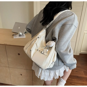 Close-up of off-white hobo bag with silver zippers and a cute white plush doll keychain