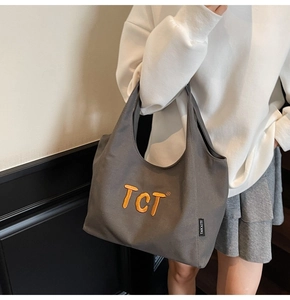 Detailed view of dark grey canvas tote bag with vibrant orange TCT embroidery and brand tag