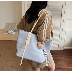 Macro shot of light blue croc-effect tote bag with cream straps and bear charm pendant