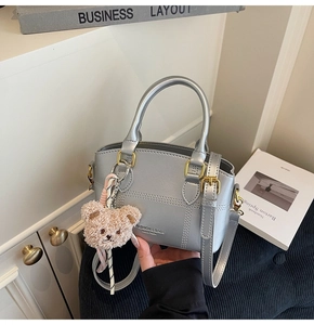Close-up of silver crossbody bucket bag with textured lines and brown teddy bear charm