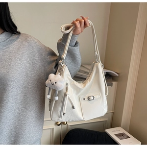 Close-up of beige glossy shoulder bag with cloud plush charm and metal buckle details