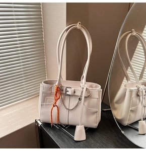 Détail du sac crème avec boucle argentée, chaîne et pendentif tissé orange via un miroir