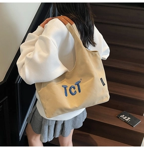 Detail of canvas tote bag with blue TCT embroidery and premium brown leather handles