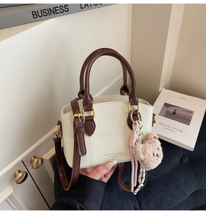 Detail of cream leather bucket bag featuring coffee handles and a brown plush bear charm