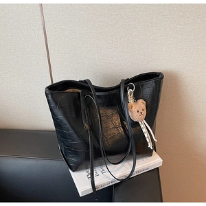 Detail of black faux leather tote with crocodile texture and cute brown plush bear charm