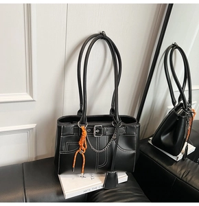 Détail du sac cabas noir avec pendentif orange et coutures contrastées sur le cuir