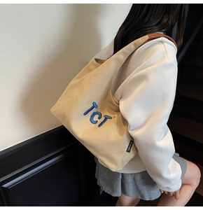 Detail view of beige canvas tote bag with blue TCT embroidery and leather reinforcements