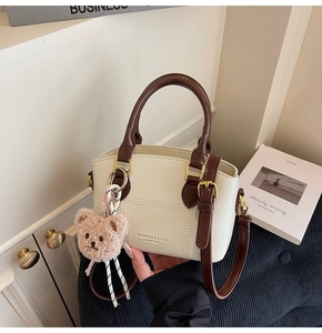 Detail view of cream leather bucket bag with brown handles and plush bear charm
