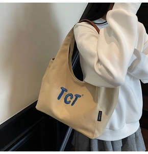 Detail view of large canvas tote bag with blue embroidery and brown leather straps