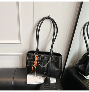 Détail du sac cabas noir avec surpiqûres blanches, chaîne argentée et breloque orange tissé