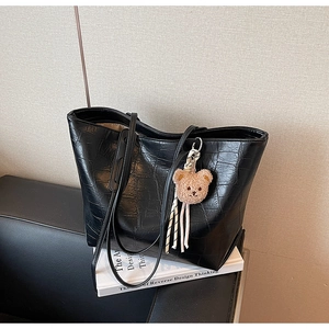 Detail of black faux crocodile leather tote bag featuring a cute brown plush bear charm