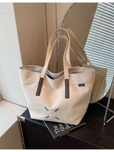 Minimalist beige canvas tote bag with brown leather accents and blue X embroidery
