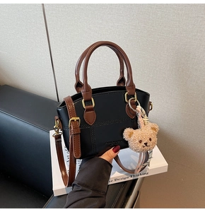 Detail of black quilted bucket bag with brown handles and a cute plush bear charm