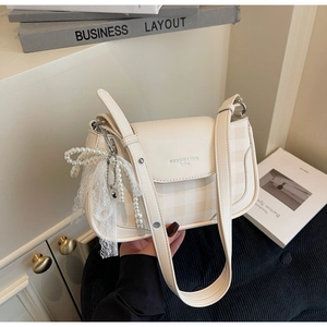 Detail of cream crossbody bag featuring plaid stitching, pearls, and lace bow charm