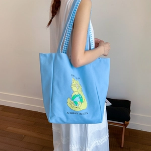 Close-up of light blue canvas tote with cartoon cat print and checkered shoulder strap