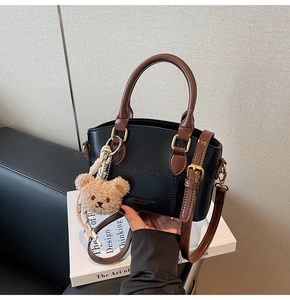 Detail of crossbody bucket bag with contrast leather and cute brown bear pendant