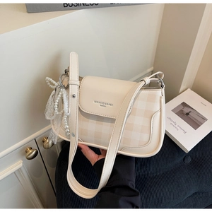 Detail of cream leather shoulder bag featuring plaid texture and pearl bow decoration
