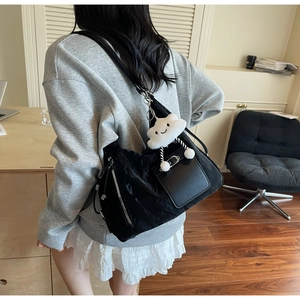 Detail of black pleated crossbody bag with a white cloud plush charm worn by a model