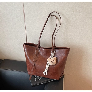 Detail of dark brown tote bag featuring crocodile texture and cute plush bear charm