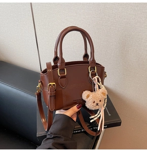 Close-up of brown vintage leather crossbody bag with stitching and plush bear charm