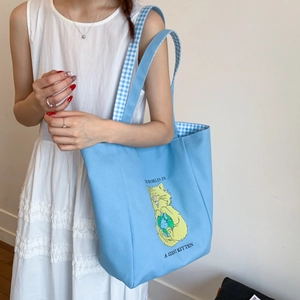Detail of light blue canvas tote bag featuring a cute cat print and plaid shoulder straps