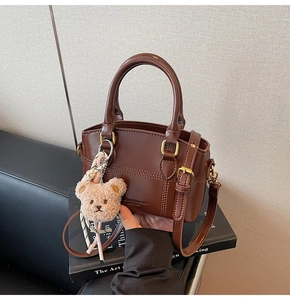 Detail of dark brown bucket bag with gold hardware and cute plush bear charm on a book