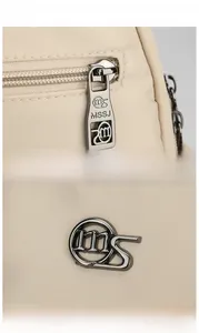 Detailed macro view of premium gunmetal zippers and brand logo on apricot Oxford backpack