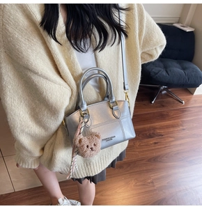 Detail of silver mini bucket bag with leather text, plush bear charm, and pink ribbon bow