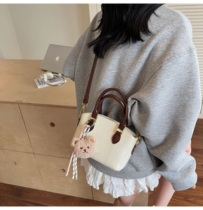Detail of cream mini bucket bag with brown handles and a cute plush bear charm accessory